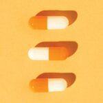 tres cápsulas de medicina alineadas verticalmente sobre fondo anaranjado, representando medicina para el tratamiento del ojo seco