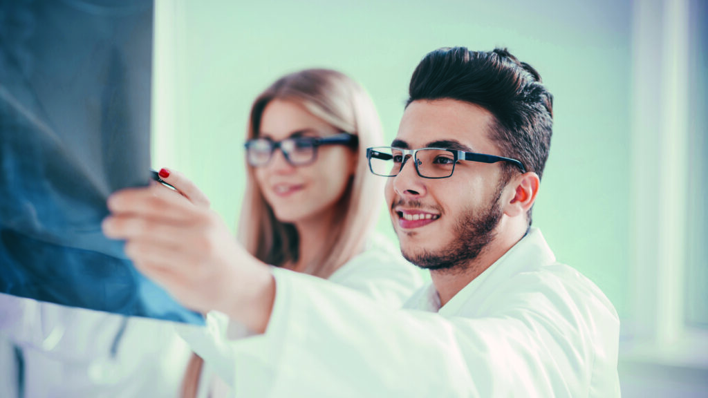 Doctor y doctora de oftalmología, jóvenes, observando sonrientes una radiografía, representando las actividades y proyecciones a futuro de la Sociedad Mexicana de Oftalmología
